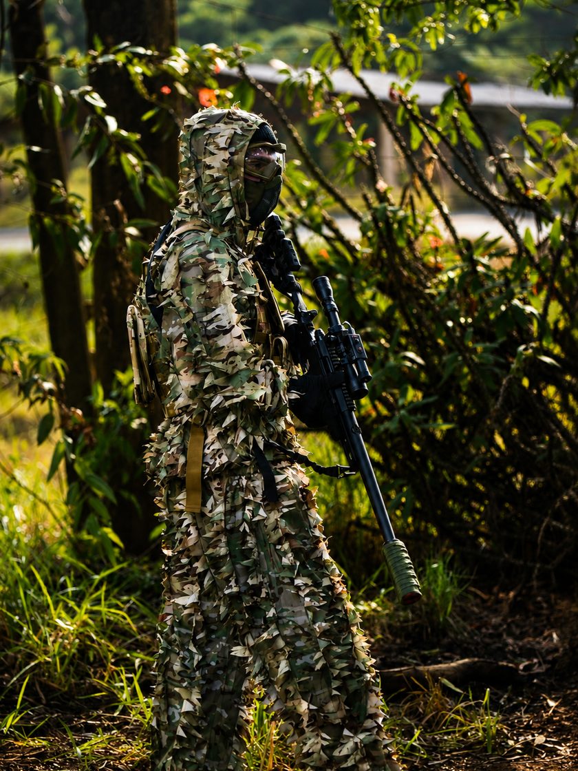 Sniper da StrikeZone em traje ghillie completo na mata